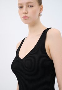 Top in cotone nero a costine con scollatura a V profonda, dotato di spalline larghe e un design in tessuto texturizzato. Forma liscia e aderente.