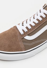 Bruna mocka- och canvas-sneakers med vita snören, kontrasterande vit randdesign, texturerad ovandel och gummisula med svarta detaljer.