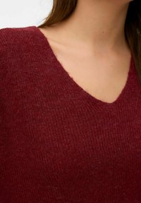 Bordowy sweter z dzianiny o kroju z dekoltem w serek, miękkiej fakturze i prążkowanym wzorze, prezentujący ciepłe, bogate odcienie kolorów.