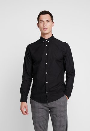 Camisa negra de manga larga con cuello abotonado, tapeta frontal con botones blancos y una textura de algodón suave.