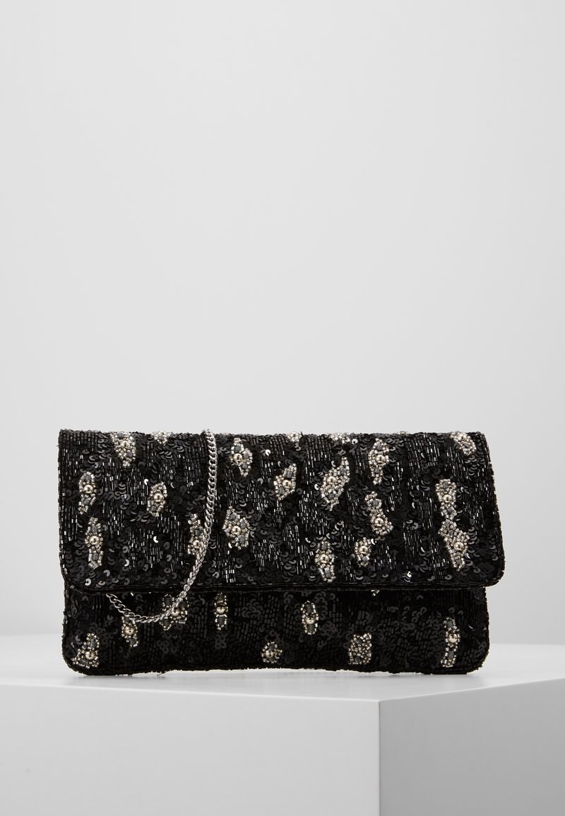 Pochette noire à sequins avec motifs floraux en perles argentées et une fine chaîne argentée, posée sur une surface blanche.