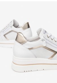 Des baskets en cuir blanc avec des accents dorés, des panneaux en mesh et une semelle blanche épaisse avec une fine bande dorée. Lacets et fermetures éclair inclus.