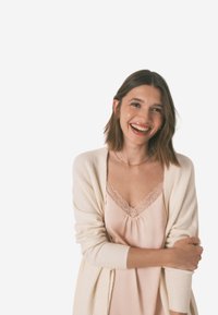 Lyserød cami-top med blonder, parret med enCreme strikket cardigan. Modellen har skulderlangt hår og smiler, mens hun krydser armene.