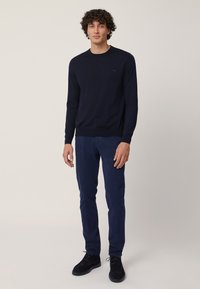 Maglione blu navy con collo rotondo, polsini e orlo a costine; abbinato a pantaloni blu navy coordinati e scarpe nere. Il tessuto appare liscio e aderente.