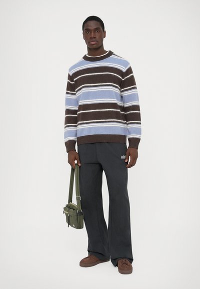 Pull en tricot rayé bleu, marron et blanc, associé �à un pantalon charbon et des baskets marron ; portant un petit sac à bandoulière vert olive.