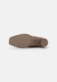 Semelle de chaussure marron avec texture lisse, bord arrondi et motif circulaire anti-dérapant au talon. Présente un design minimaliste et une signalétique subtile.
