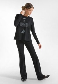 Schwarzes Langarmshirt mit weißem Text und floralem Design, kombiniert mit schwarzen Schlaghosen und schwarzen Schuhen. Glatte Textur, lässige Passform.