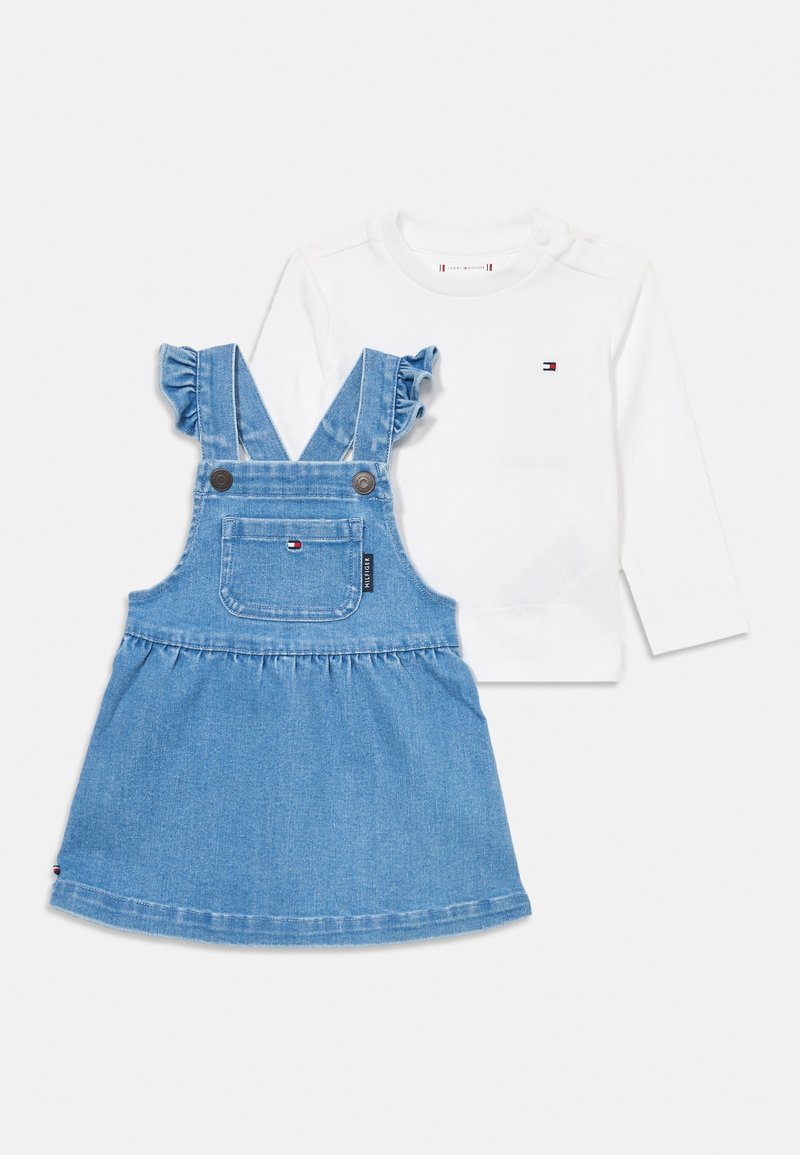 Hvit langermet skjorte med lite logo, kombinert med blå denim overallkjole med volanger på stroppene og frontlomme med logo.