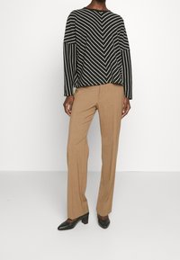 Suéter de rayas blanco y negro de manga larga combinado con pantalones beige de corte tailored y zapatos de tacón negros. Patrón geométrico en el suéter.