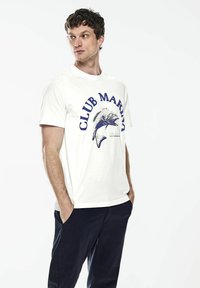 Bílá bavlněná tričko s modrou grafikou "CLUB MARINA" a ilustrací ryby, nošené s námořnickými kalhotami, s krátkými rukávy a kulatým výstřihem.