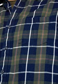 Camicia di flanella a quadri con tonalità di blu, verde e arancione, dotata di frontale con bottoni e una tasca sul petto. Tessuto testurizzato.