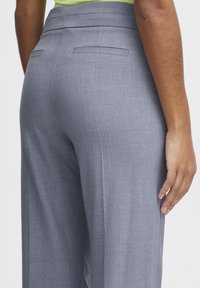 Pantalon gris sur mesure avec une texture lisse, un design à plat et deux poches arrière. Le tissu semble léger et formel.