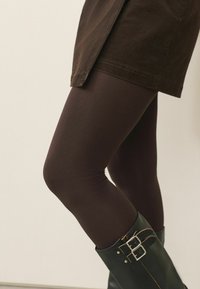 Brown leggings made of a textured material, paired with knee-high black leather boots featuring silver hardware accents. Brown corduroy skirt.