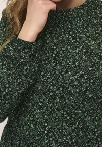 Blusa de estampado floral verde con un cuello fruncido. Presenta un fondo oscuro y delicados motivos de hojas y pájaros. Textura de tela suave.