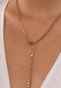 Goldene Halskette mit runden Gliedern, einem runden Anhänger und einem Lariatschnitt, der vom Verschlussbereich herunterhängt.