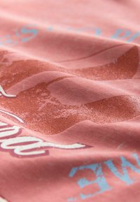Textile in coral pink with distressed blue and sparkly orange accents. Wavy patterns and lettering create texture on soft fabric.
