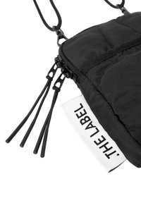 Black quilted pouch with a zipper, adjustable black drawstring straps, and a white label with black text reading "THE LABEL."