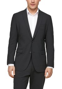 Zwarte colbert van gladde stof, met twee voorzakken, een enkele knoopsluiting en gesneden revers over een wit shirt.