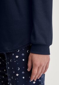 Marineblauwe sweatshirt met een kantafwerking en geribde manchetten, gecombineerd met gestreepte marineblauwe pyjamabroek met witte en lichtblauwe manen en planeten.