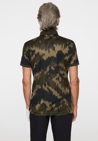 Kortärmad polo skjorta i mörkgrön med kamouflage mönster. Har en krage och är gjord av ett mjukt, lätt tyg.