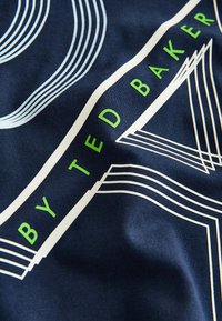Laivastonsininen kangas, jossa vihreät "BY TED BAKER" kirjaimet ja valkoiset geometriset viivakuviot teksturoitulla pinnalla.