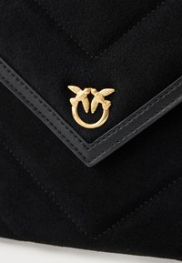 Borsa a mano nera in suede con un design a zigzag, hardware dorato a forma di uccello e tessuto testurizzato con accenti in pelle a contrasto.