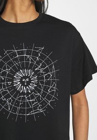 Camiseta de algodón negra con diseño gráfico en blanco de un sol y un patrón de constelaciones, mangas cortas y escote redondo.