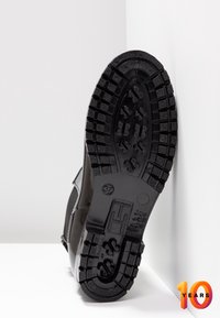 Suela de goma negra de un zapato con un patrón de textura en la banda de rodadura, lados lisos y detalles grabados en la suela.