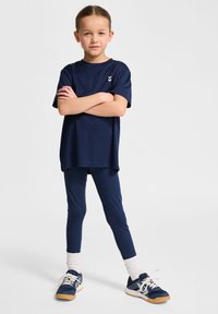 T-shirt de sport bleu marine à manches courtes et encolure ras du cou, associé à des leggings assortis et des baskets avec des accents et des lacets blancs.