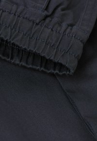Svart tyg med rynkad midjebandsdetalj, slät textur och synliga sömmar, vilket antyder en elastisk och åtsittande design.
