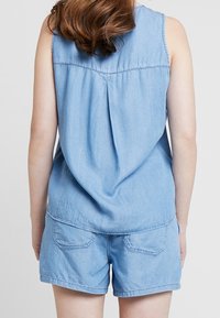 Ljusblå denimlinne utan ärmar med sammanknäppt baksida och rundad nederkant, i par med matchande denimshorts med bakfickor.