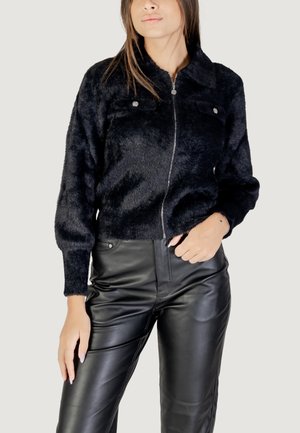 Giacca nera fluffy con zip e colletto, due tasche anteriori e polsini a coste, abbinata a pantaloni in ecopelle nera eleganti.