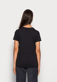 Camiseta de algodón negra de manga corta y cuello redondo, mostrada desde la parte de atrás, combinada con pantalones de pijama a cuadros.