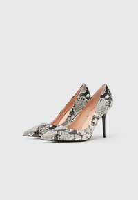 Et par høyhælte sko med spiss tå, med et svart og hvitt slangeskinnmønster og slanke stiletthæler på en enkel hvit bakgrunn.