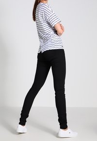 Camiseta blanca con finas rayas negras, combinada con pantalones ajustados negros y zapatos de tela blancos. El conjunto presenta un corte relajado y un diseño simple.