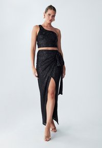 Black sequin two-piece outfit featuring a one-shoulder crop top and a high-slit wrap skirt with a tied accent on one side.