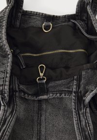 Schwarze Denim-Tasche mit strukturiertem Äußeren, ausgestattet mit einer goldenen Reißverschlusstasche und silbernen Hardware-Akzenten. Innenfutter aus schwarzem Stoff.