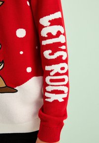 Rød strikket sweater med "LET'S ROCK" i store hvide bogstaver på ærmet, med et sne-tema design og en hvid bundkant.
