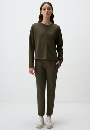 Pullover verde oliva a maniche lunghe con cucitura frontale, abbinato a pantaloni slim-fit coordinati. Entrambi realizzati in tessuto morbido ed elastico; inclusi sneakers.