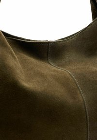 Bruine suède handtas met een zachte textuur, gebogen vorm en zichtbare stikseldetails langs de naden voor structurele ondersteuning en design.