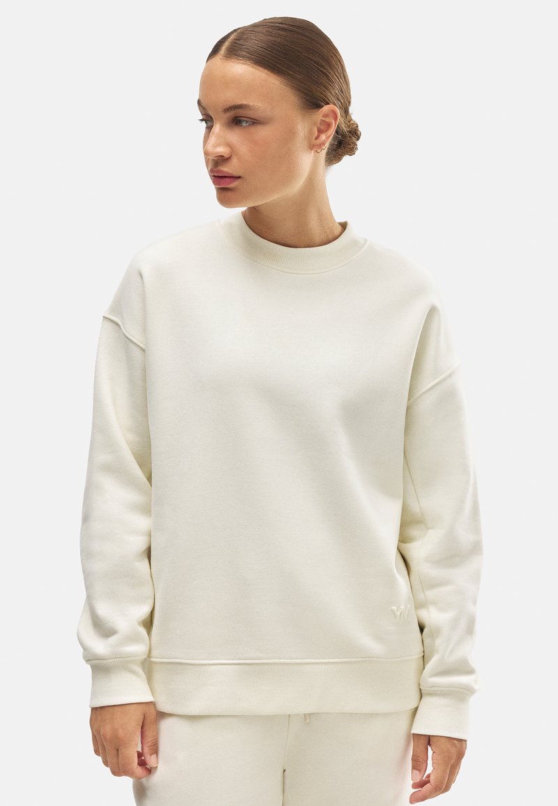 Sudadera de color crema hecha de una tela suave, con cuello redondo, hombros caídos y puños y dobladillo acanalados.