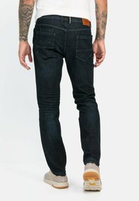 Donkerblauwe denim jeans met een slim fit, voorzien van achterzakken en een leren label op de tailleband. De textuur is glad met een lichte stretch.