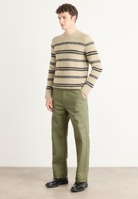 Beige striped knit sweater with black stripes, paired with olive green pants and black shoes. The materials appear soft with a textured finish.