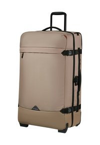 Beige soft-shell wheeled suitcase with telescopic handle, side handles, compression straps, and front zipped pocket.