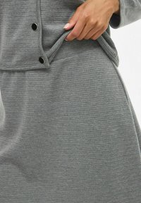 Tissu en tricot côtelé gris avec une texture lisse. Présente un design superposé avec des boutons-pression, mettant en valeur un style de vêtement superposé.