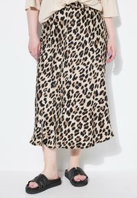 Beige midi-jurk met luipaardprint en zwarte en bruine vlekken. Soepele textuur, uitlopende vorm, elastische tailleband. Gecombineerd met zwarte instapsandalen.