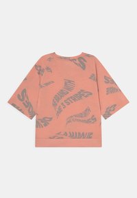 Růžové tričko s krátkými rukávy a volným střihem, zdobené vlnitým šedým grafickým textovým motivem po celém povrchu. Hladká bavlněná textura, kulatý výstřih.