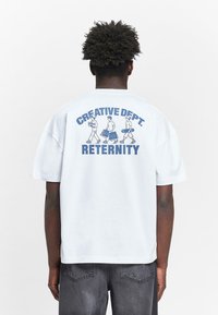 Weißes Kurzarm-T-Shirt mit einem blauen Grafikdruck auf dem Rücken, der "CREATIVE DEPT." über Illustrationen von drei Figuren und "RETERNITY" darunter zeigt.