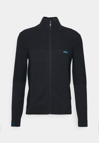 Svart zip-up jacka med texturerade axlar, kontrasterande blå accenter och logotyp. Har en hög krage och ribbade ärmslut.