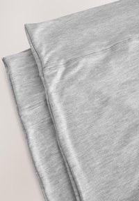 Leggings en tissu gris clair pliés avec détails de couture visibles sur un fond neutre.